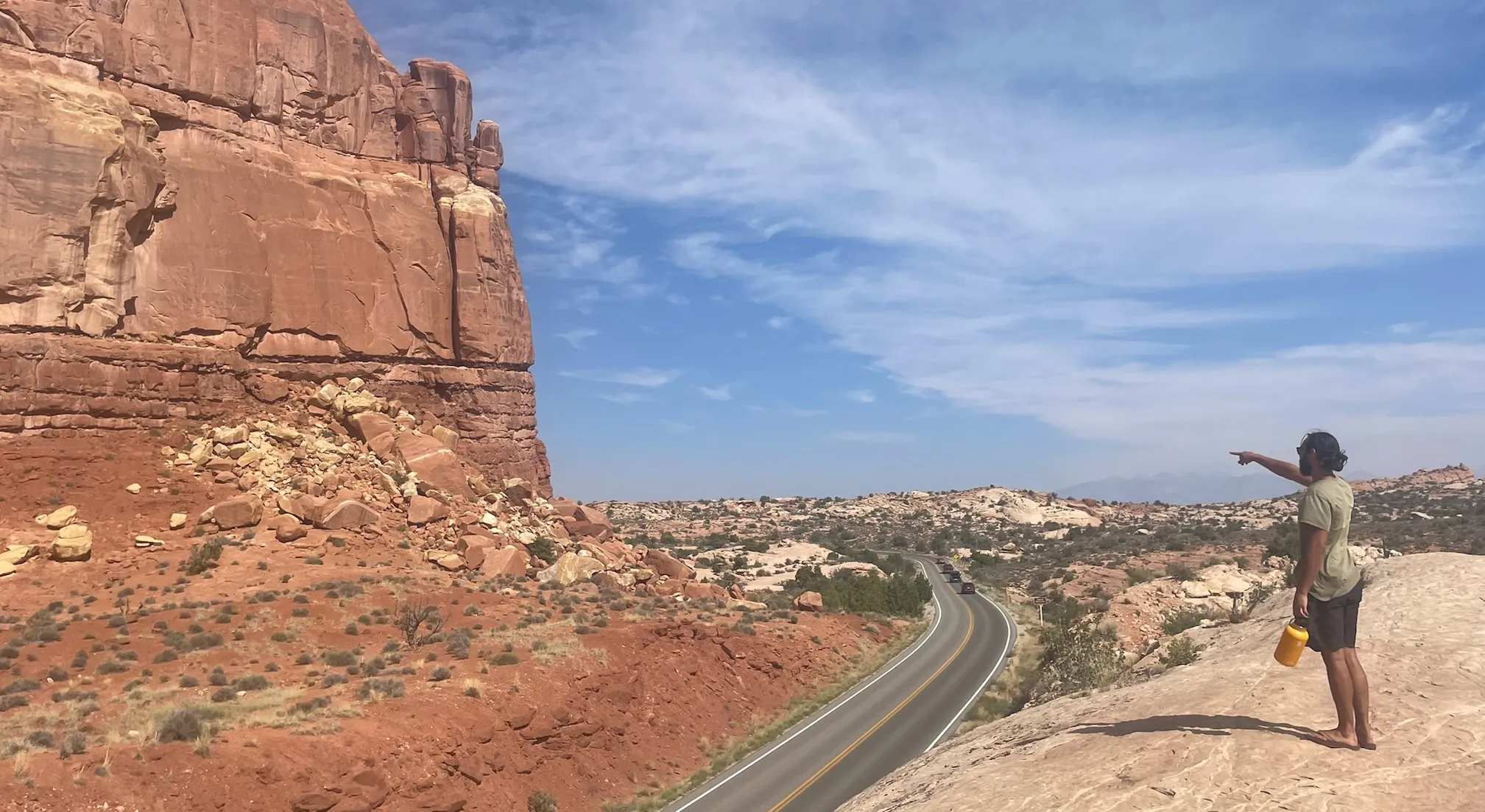 A photo of CJ pointing at something in the distance. He is standing on a red rock in arches national park.